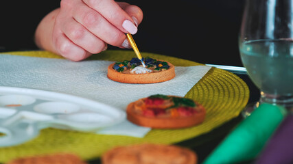 Fototapeta na wymiar Cookies art decorating: woman painting cookies with brush and food colors on palette