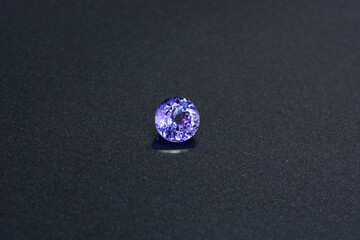 Natural tanzanite gemstone. Round faceted, shaped, transparent, bluish violet color, clean gem setting for making jewelry. Gemology theme. Dark background. 