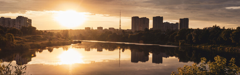 Naklejka premium Golden epic contrast summer sunrise panorama in city landscape with reflection in lake mirror water surface. Oleksiivske Reservoir and TV tower silhouette, Oleksiivka district in Kharkiv, Ukraine