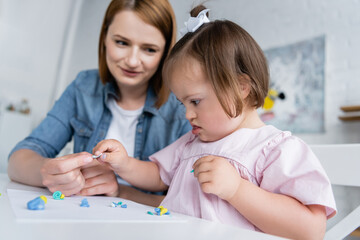 blurred kindergarten teacher molding plasticine with disabled kid with down syndrome