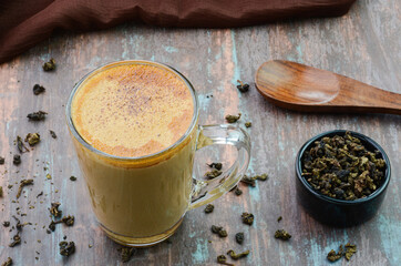 Tea latte in a glass cup with dried tea leaves in a bowl