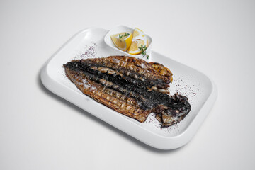 closeup of grilled mackerel fish with lemon on plate on white background