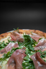 closeup of italian pizza with prosciutto, arugula and cheese on black background