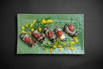 top view of eggplant rolls with cream cheese on green plate on black background