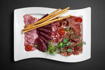 top view of cold meat plate with salami, prosciutto, sausage and bread sticks