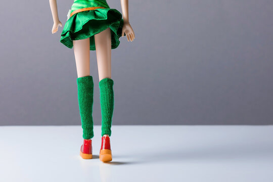 A back view faceless doll in a short  skirt  in green leggings standing against grey wall.  Anti-cellulite concept, sport activity.