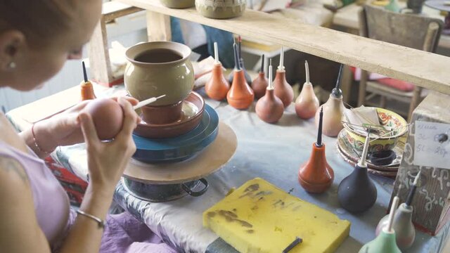 Female Potter painting clay pot on spinning wheel using special bulb aplicator