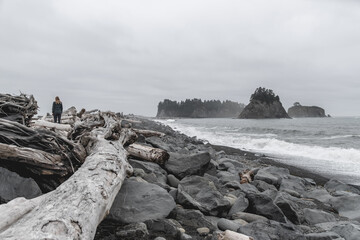 Young woman walking among rocks and driftwood on Rialto Beach in Olympic National Park