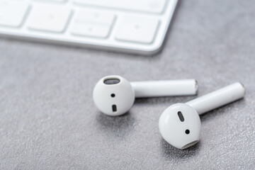 Modern wireless white bluetooth headphones with charging case near bluetooth keyboard on gray table