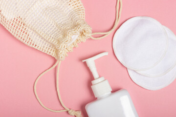 Cotton reusable make-up remover pads in a cloth bag and face wash and cleanser on a pink background. The concept of ecology and conscious consumption. Reusable cotton pads