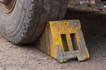 Old dirty yellow wheel chock under the wheel of a parked truck. Device for safe parking of a car