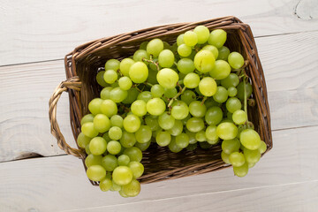 One bunch of organic ripe seedless grapes in a basket, on a wooden table, close-up, top view.