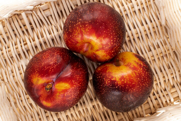 Three juicy ripe plums in a basket of vines, close-up, top view.