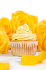 Vanilla cupcake with yellow frosting surrounded by yellow roses