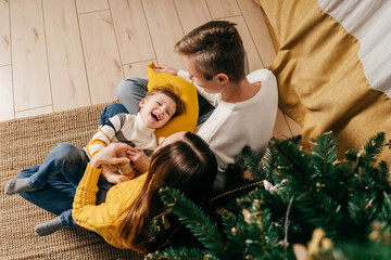 Mom, dad tickle son near christmas tree