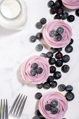 Homemade vanilla cupcakes with blueberry buttercream and fresh blueberries on top on a white marble background