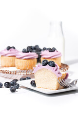 Homemade vanilla cupcakes with blueberry buttercream and fresh blueberries on top on a white marble background