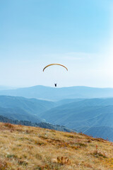 Paragliding in mountains. Freedom to fly in air over mountains with parachute. Paragliding behind blue sky Carpathian Mountains hills range landscape. Active tourist sport People fly using Parachute.
