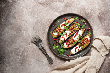 Grilled eggplants with yogurt sauce and pomegranate on a brown grunge background. Top view, flat lay. Middle Eastern and Mediterranean healthy food.