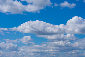 Many white fluffy cumulus clouds on bright summer blue sky. Cloudscape, overcast.