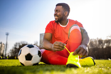 Naklejka premium happy multicultural hispanic soccer player smiling and wear red sporty suit outdoor sunny day