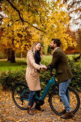 Fototapeta na wymiar Young couple in the autumn park with electrical bicycle