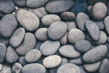 Dark moody textured background of smooth pebbles.
