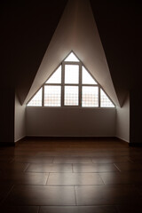 Loft, ático vacío con suelo de madera, paredes blancas y ventana triangular de vidrio. Lugar...