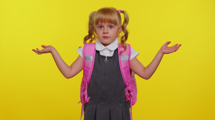 I dont know what to say. Confused schoolgirl with backpack feeling embarrassed about ambiguous question, having doubts, no idea, being clueless and uncertain. Yellow studio background. Back to school