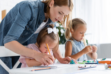 teacher assisting disabled child with down syndrome drawing near blurred child in private...