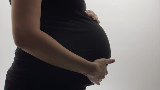 pregnant young woman on studio background stroking her tummy with hands, expecting mother, happy motherhood concept