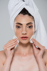woman with towel on head applying tonic with cotton pads isolated on grey