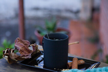 Black mug with tea on a balcony table with leaves and a brick wall in the blurred background