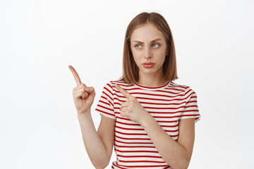 Skeptical and suspicious young blond woman, looking and pointing left at smth strange uncertain, having doubts, being hesitant and unsure about something, white background
