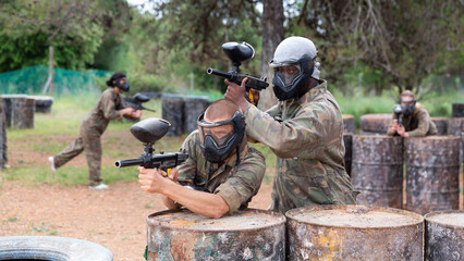Fototapeta premium Two paintball player in camouflage and mask aiming with gun in shootout outdoors