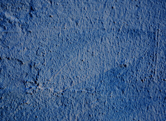 Fototapeta na wymiar Rough, unevenly colored plaster on the dark blue wall.