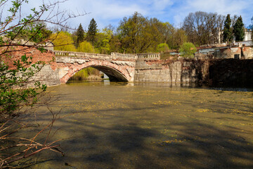 Fototapeta na wymiar Old arched brick bridge across a pond in Sharovka Palace park in in Kharkov region, Ukraine