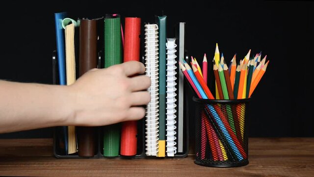 The hand takes one folder on the table and puts it back. The man selects a notebook from a pack. Take and put the diary in place. Diaries in a bookstand.