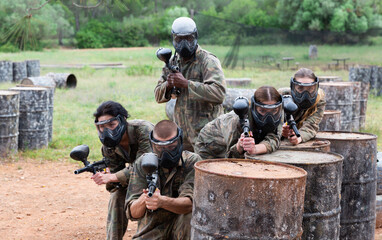 Fototapeta premium Five paintball players in camouflage and protective masks aims with guns outdoors