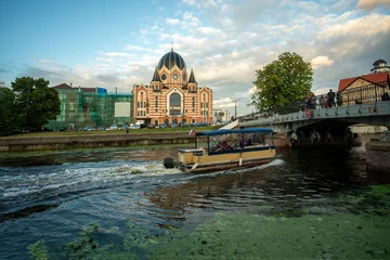 Deurstickers Summer panorama with Synagogue in Kaliningrad and moving boat in chanal and bridge to island ( with Cathedral) © Marat Lala