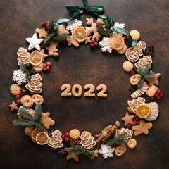 Creative Christmas wreath of assorted cookies, cinnamon, anise stars, berries with date 2022 inside on brown background. New Year. Top view. Xmas holiday greeting card. Copy space.