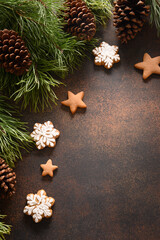 Christmas homemade assorted glazed cookies and frame of fir tree and cones on brown background. New Year holiday treats. Xmas vertical greeting card with copy space.