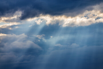Fototapeta na wymiar Sunbeams breaking through dark clouds. Stormy sky and sun rays. Epic view of natural background.