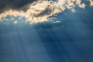 Sunbeams breaking through dark clouds at sunset. Stormy blue sky and sun rays. Epic view of natural background.