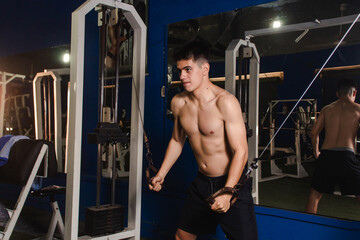 Fototapeta na wymiar Young fitness guy training chest with pulley in the gym.