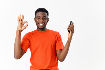 African American in an orange t-shirt with a phone in his hands shows a finger light background