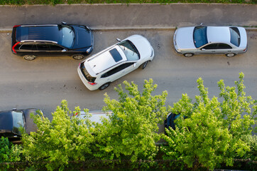 The uneasy parking of the white car near black and grey, shot from above. Parallel parking on the...
