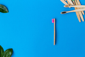 Creative composition with Eco-friendly Bamboo Toothbrushes and green leaves, on blue background with copyspace for text or presentation. 