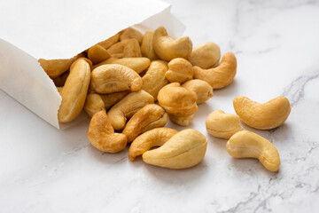 Many cashew nuts on marble background out of white paper packet. Source of natural fats and protein. Healthy eating or diet concept.