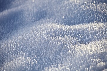 White ice crystals in bright sunlight. Macro photography of ice crystal texture. Snow crystals close-up on a bright frosty winter day. White sparkling snow surface close up. Abstract snowy pattern.